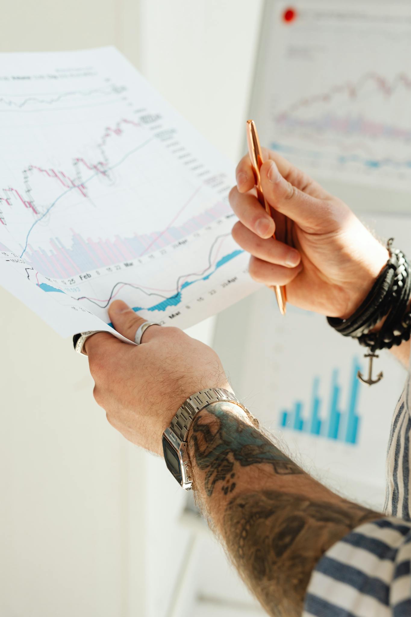 Close-up of a person's hands holding financial charts and graphs with a pen.